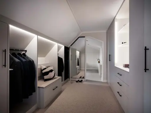 En stilren walk-in-closet med inbyggd sittbänk och garderobslösningar som utnyttjar kattvindens vinklar.