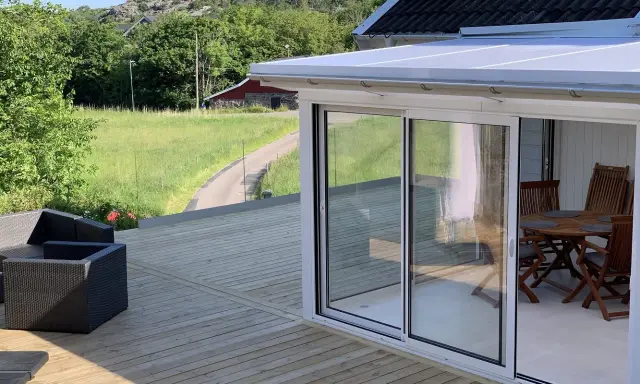Nybyggd veranda med glaspartier och tak, perfekt för att bygga en mysig uteplats. Utsikt över grönskande landskap.