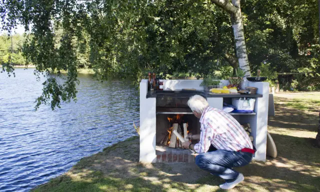 Man tänder en murad grill vid en sjö.