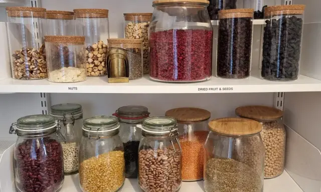 Välordnat skafferi med glasburkar fyllda med nötter, torkad frukt, frön och baljväxter. Perfekt för att organisera skafferi.