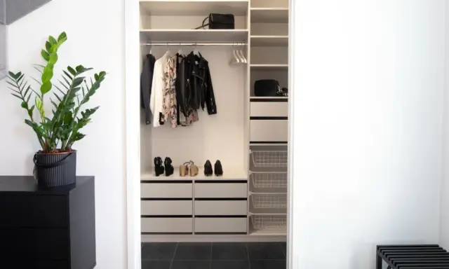 En stilren liten walk in closet med kläder, skor och väskor. En grön växt på en svart byrå ger liv.