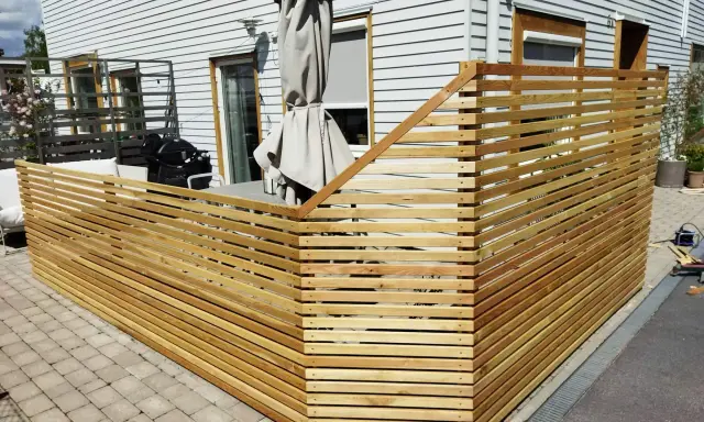 Nybyggt staket i trä ramar in uteplatsen. Grillen och parasollet syns bakom.