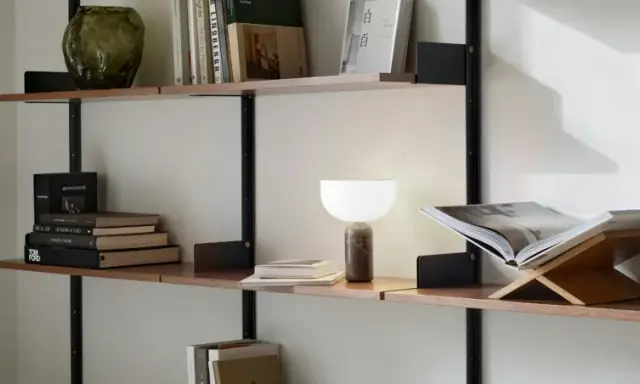En stilren hylla i vardagsrummet med böcker, en vas och en lampa.