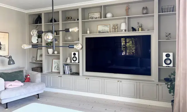 En platsbyggd bokhylla i vardagsrummet med en stor TV i mitten. Hyllorna är fyllda med böcker, dekorationer och växter.
