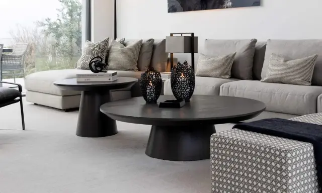 Ett modernt vardagsrum med en stor, mörk soffa och ett elegant, runt soffbord. Två svarta ljuslyktor står på soffbordet.
