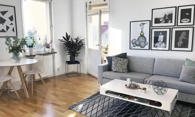 Mysig etta med grå soffa, vitt soffbord och en rund matplats. Konst på väggarna ger personlighet.