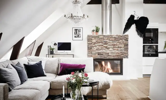Mysigt vardagsrum med öppen spis, soffa och ett soffbord i 3 delar med blommor och ljus.