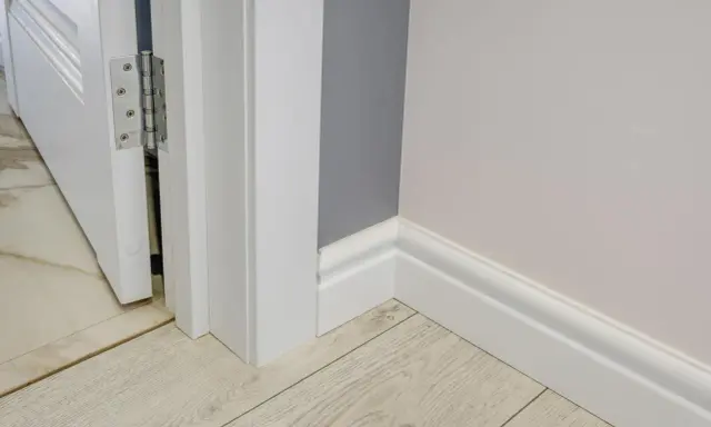Nymålade vita snickerier runt en dörröppning och längs väggen. Golvet är ljust träliknande laminat.
