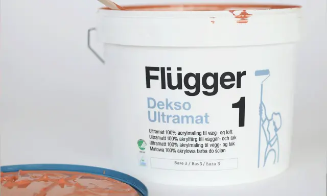En hink Flügger Dekso Ultramat färg, med en träpinne som rör om. Jämför sidenmatt vs matt finish.
