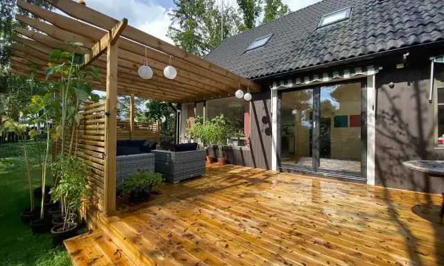 Träaltan med pergola och loungegrupp ger härlig altan inspiration. Solrosor och grönska ramar in.