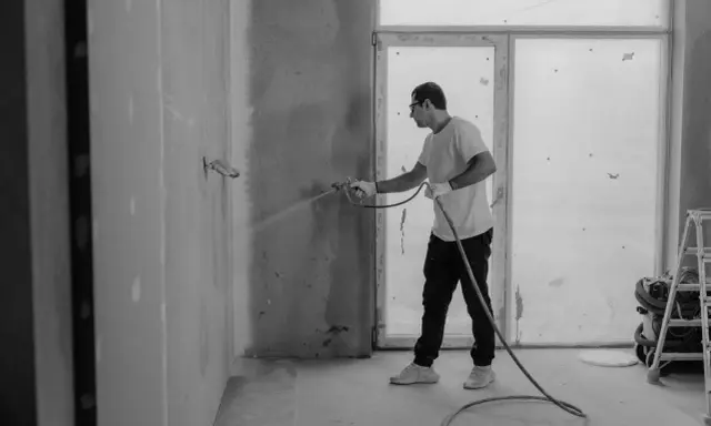 Man sprutar färg på en vägg inomhus, en del av arbetet med fasad hus.