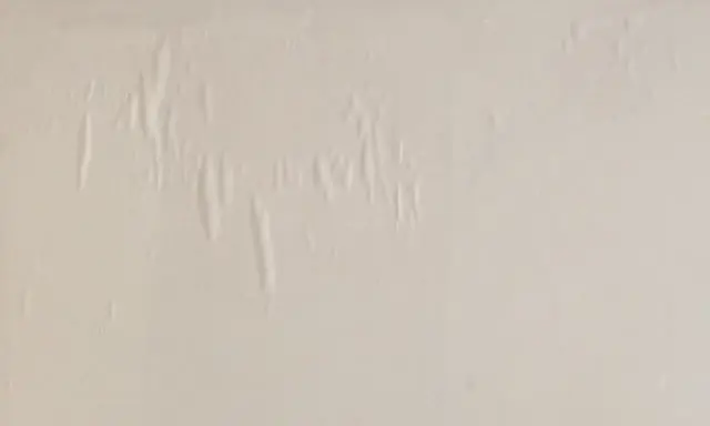En vit vägg med bubblor och veck i tapeten, som om någon försökt tapetsera på tapet.