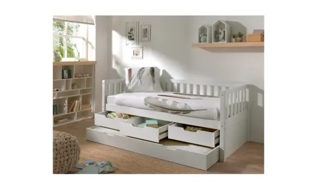 Vit barnsäng med förvaring i form av lådor under. Sängen har en vit sänghimmel och en kudde med fjäderprint.