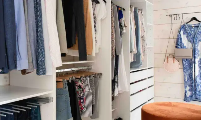 En walk-in closet med kläder på galgar, lådor och en blåvit klänning på väggen.