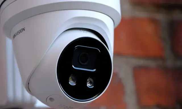 Vit övervakningskamera med Hikvision-logotyp, monterad mot en tegelvägg. Ger trygghet med larmklass 1.