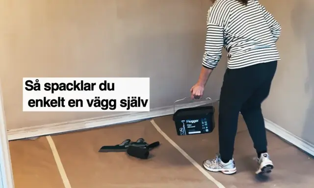 Person med hink med spackel och verktyg för att slipa och jämna ut en vägg.