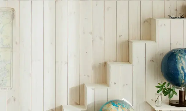 En vägg med ljus träpanel ger en mysig känsla. En gammal sjökarta hänger på ena sidan, medan en trappliknande hylla på andra sidan visar upp jordglober och böcker. Perfekt panel inomhus inspiration för äventyrliga själar.