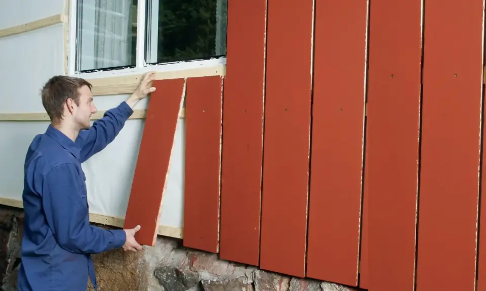Man monterar en röd träpanel på en fasad. En dropplist syns under fönstret.