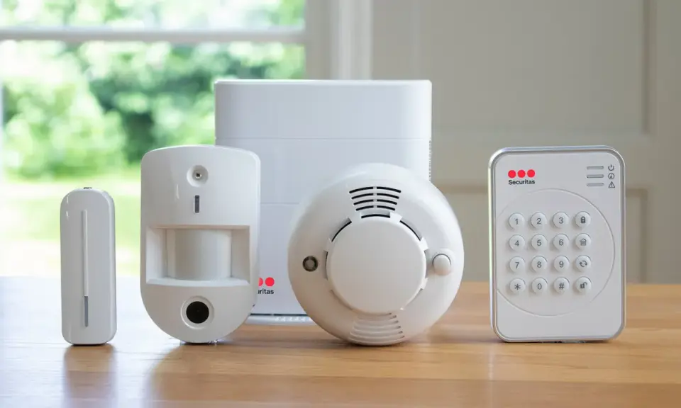 En uppsättning säkerhetskomponenter: en rörelsedetektor, en dörr-/fönstersensor, en rökdetektor och ett kontrollpanel med knappsats. Allt redo för att ge en alert alarm.