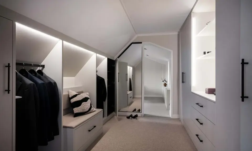 En stilren walk-in-closet med inbyggd sittbänk och garderobslösningar som utnyttjar kattvindens vinklar.