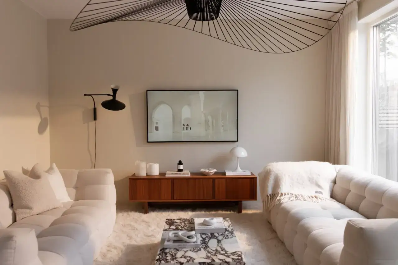 Ett modernt vardagsrum med vita soffor, en marmorbänk och en stor taklampa. Väggarna är målade i en ljus nyans, vilket ger en lugn och inbjudande atmosfär.