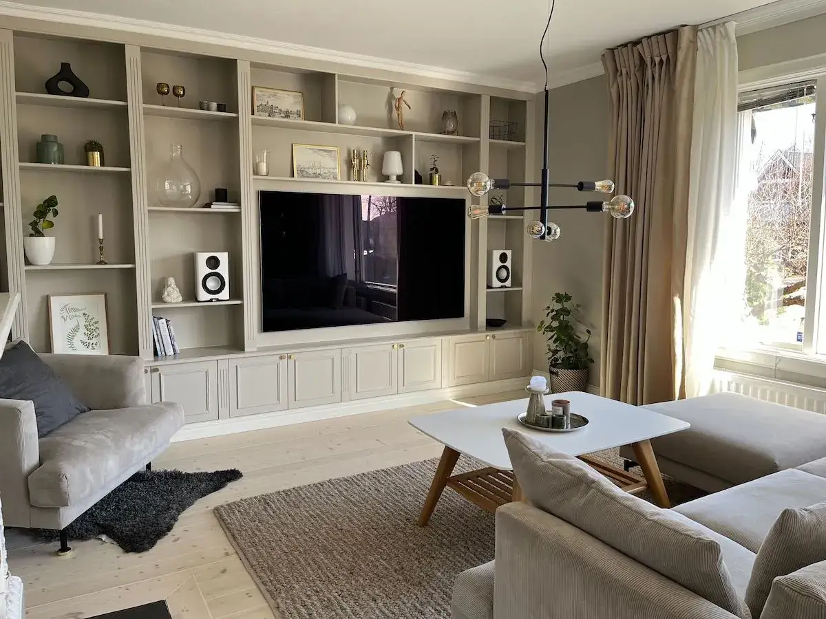 En elegant platsbyggd bokhylla i vardagsrummet med en stor TV, h&ouml;gtalare och dekorativa f&ouml;rem&aring;l.