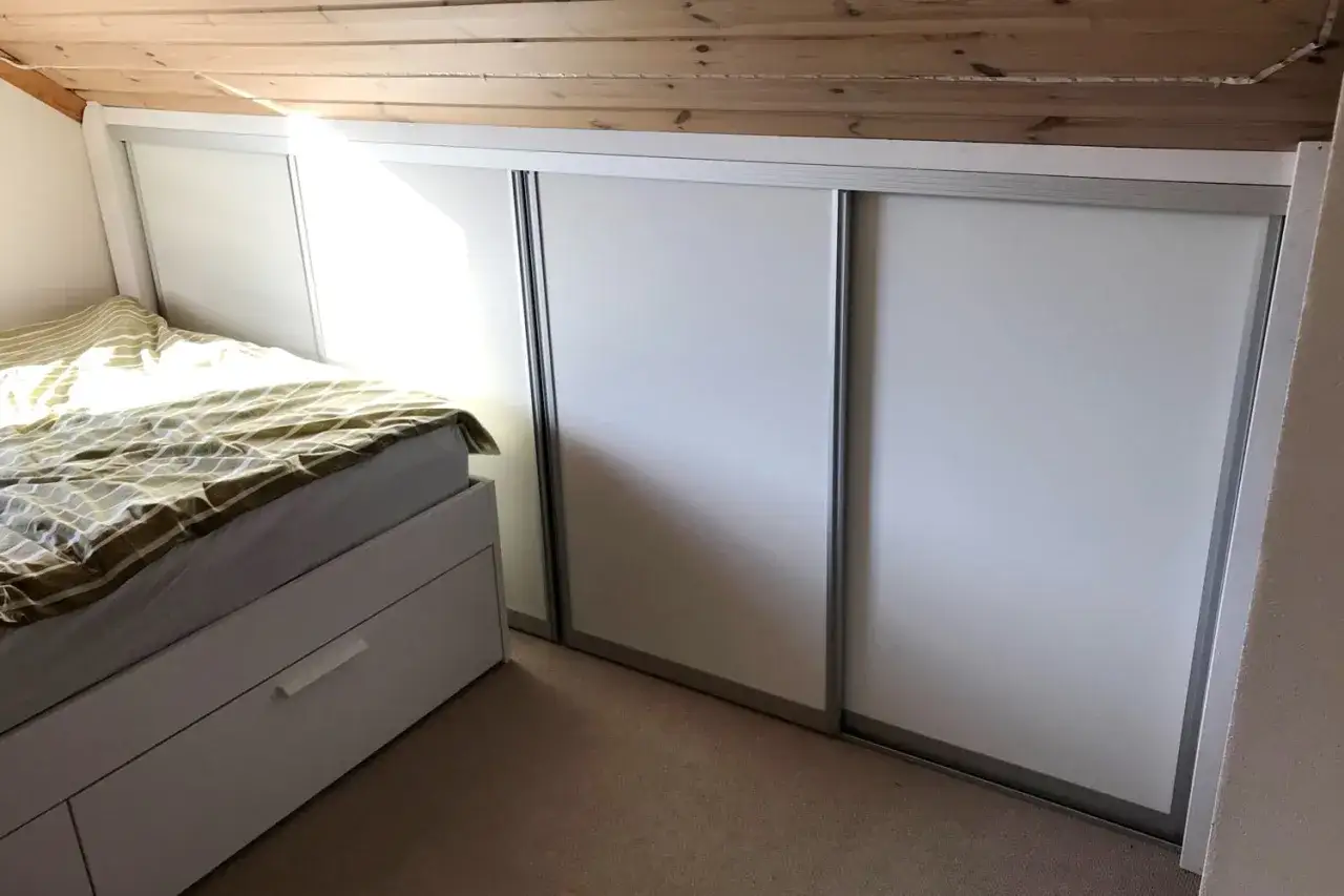 S&auml;ng med l&aring;dor och vita skjutd&ouml;rrar under snedtaket. Perfekt kattvind inspiration f&ouml;r smart f&ouml;rvaring.