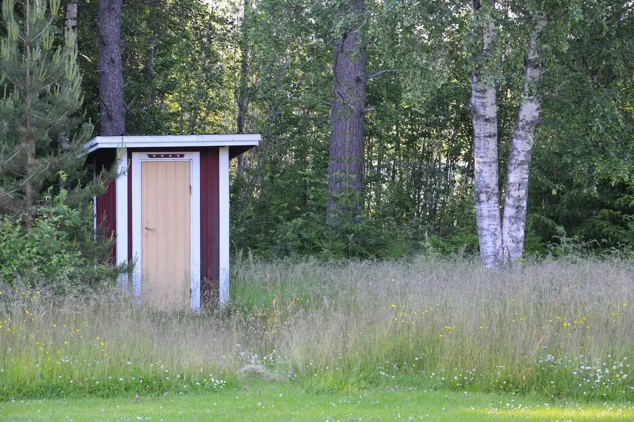 R&ouml;tt utedass med gul d&ouml;rr, omgivet av h&ouml;gt gr&auml;s och tr&auml;d. Kanske finns det utedass regler att f&ouml;lja h&auml;r.