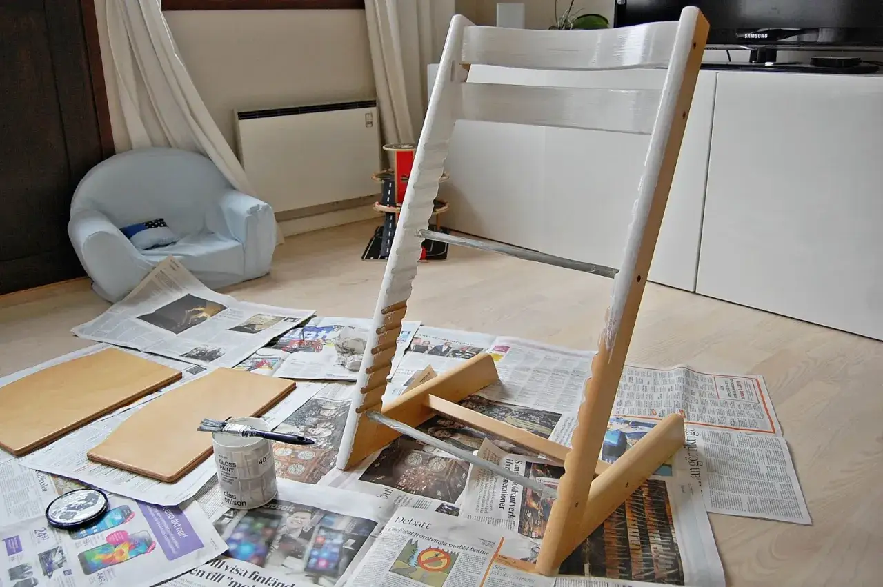 M&aring;la om Stokke stol med vit f&auml;rg. Tidningar skyddar golvet. Nya tr&auml;delar ligger redo.