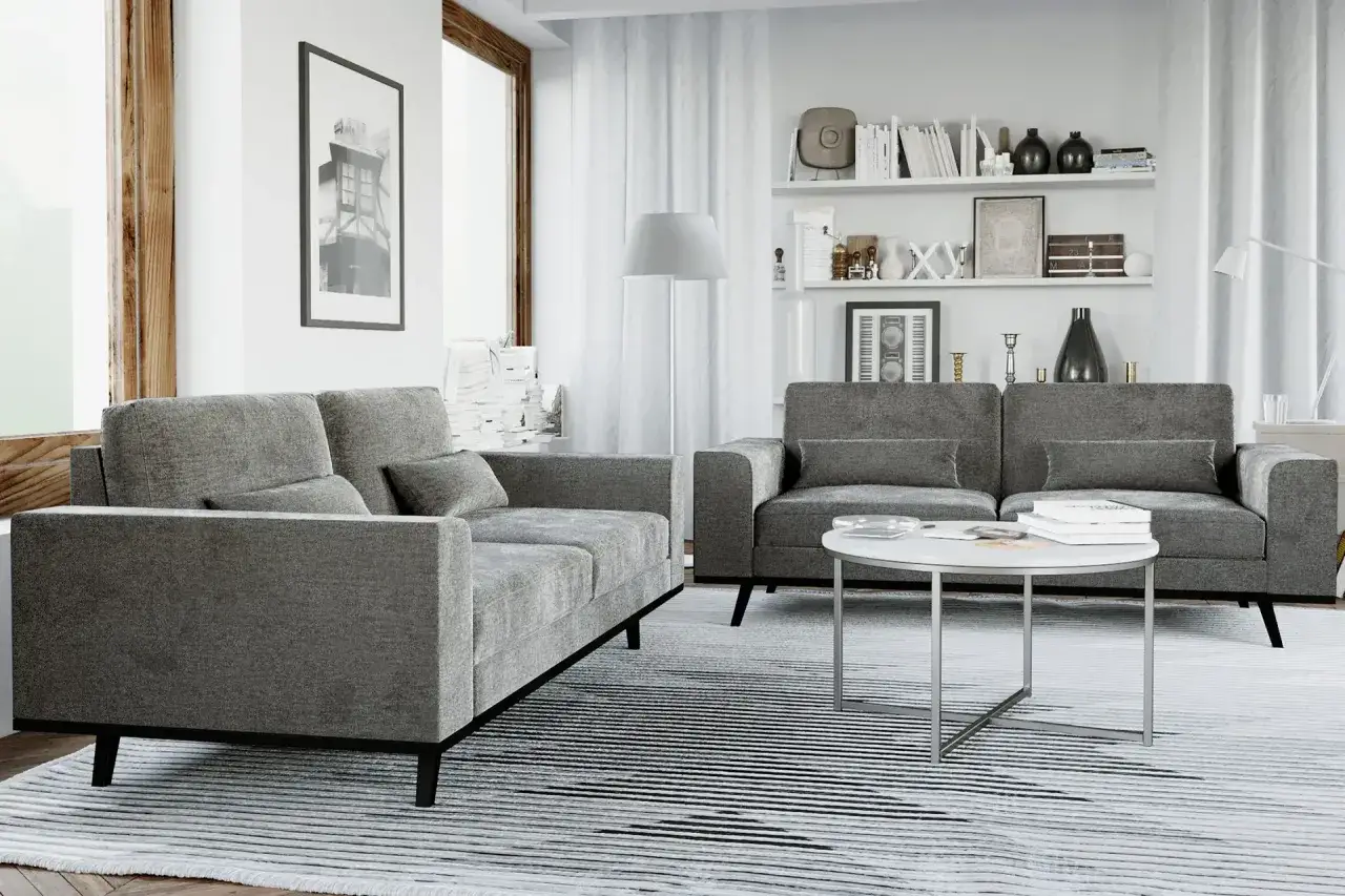 En modern soffgrupp 3+2 i grått tyg med ett runt soffbord framför. En stor fönster och bokhyllor i bakgrunden.
