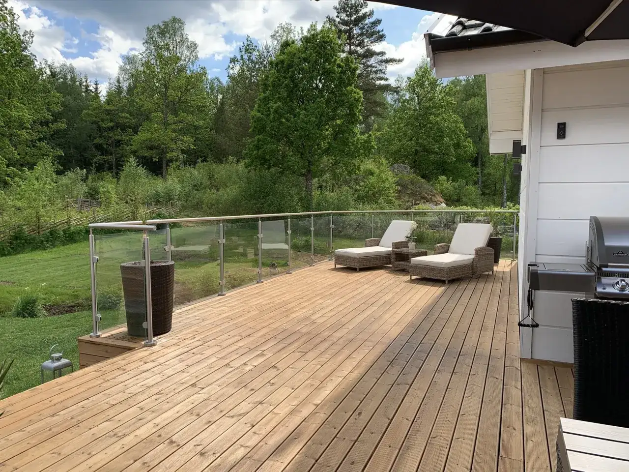 En nybehandlad altan med solstolar och grill, omgiven av grönskande natur. Perfekt för avkoppling.
