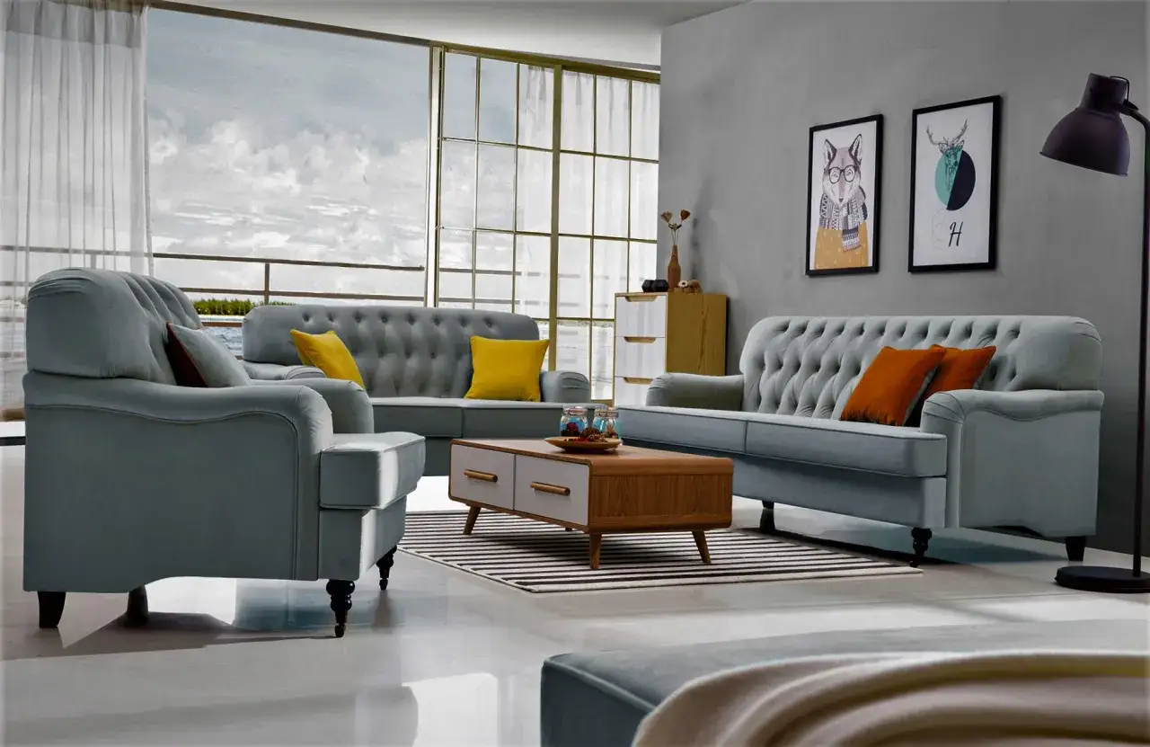 En elegant soffgrupp 3+2+1 i ljusgrått sammet med gul och orangea kuddar. Ett modernt soffbord och konst på väggen.