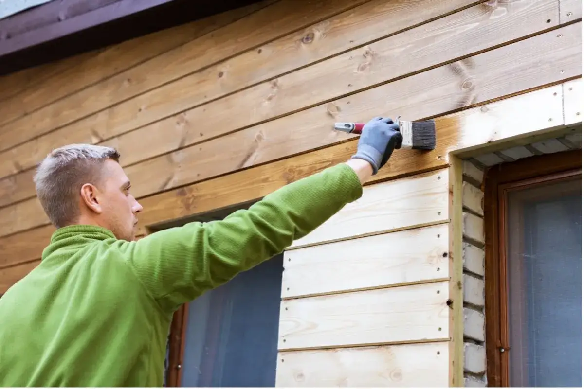 Man m&aring;lar panel utomhus med en pensel. Tr&auml;fasaden f&aring;r ny f&auml;rg.