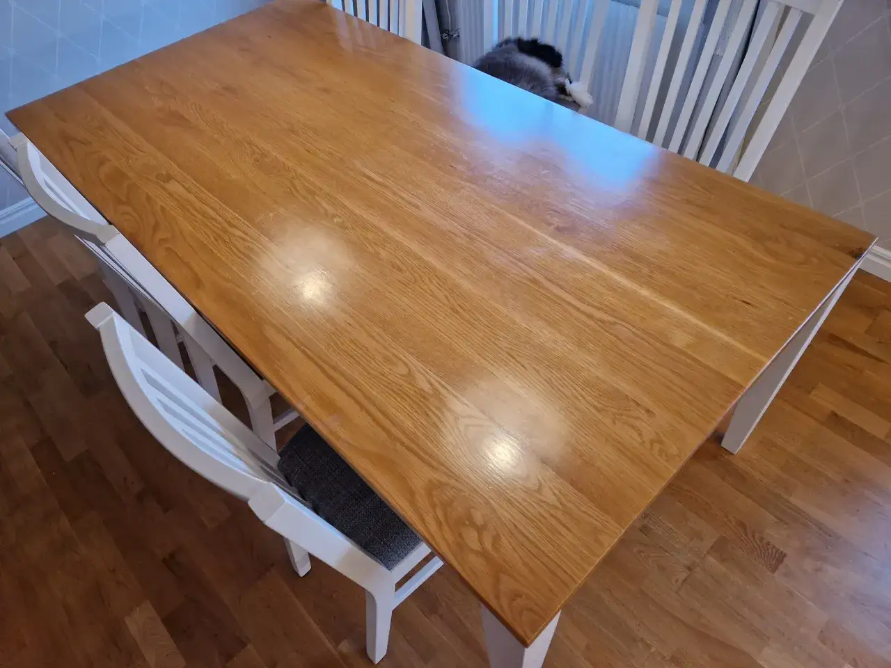 Ett träbord med ljus bordsskiva och vita stolar. Kanske dags att måla bordsskivan för en ny look?